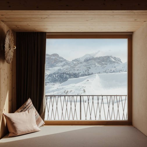 Cozy, bright relaxation corner with soft, cuddly pillows and an adjacent window front that offers a wonderful view of the snow-covered Dolomites.