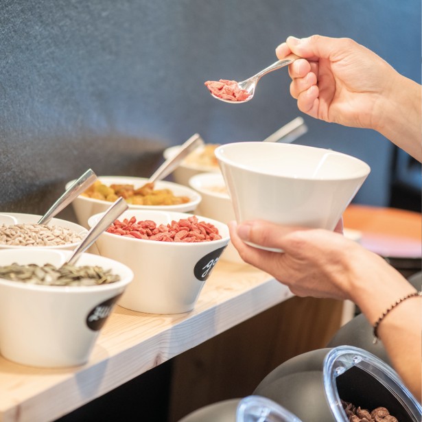 Una persona tiene una ciotola e si serve dai vari tipi di cereali e muesli del buffet della colazione.