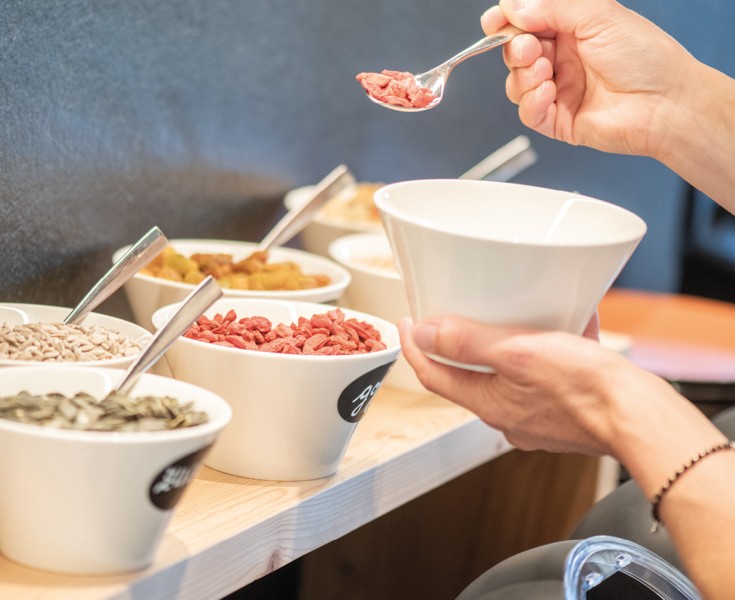 Una persona tiene una ciotola e si serve dai vari tipi di cereali e muesli del buffet della colazione.
