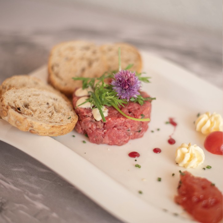 Tartare di manzo presentata in modo invitante con pane, un po' di burro e due fette di pomodori.