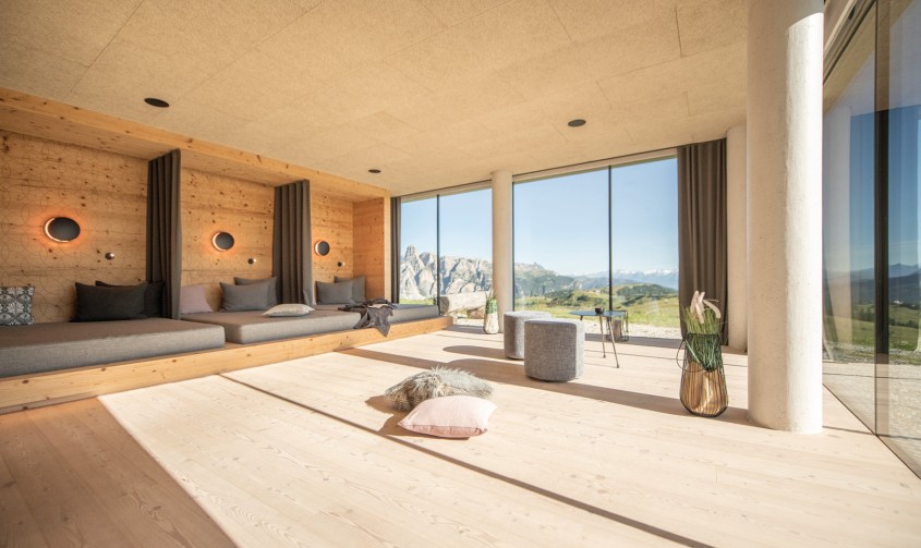 Der Ruheraum ist mit viel Holz ausgekleidet und bietet mehrere Ruhemöglichkeiten mit Polstern. Die großen Fensterfronten geben den Panoramablick auf die umliegenden Berge frei.