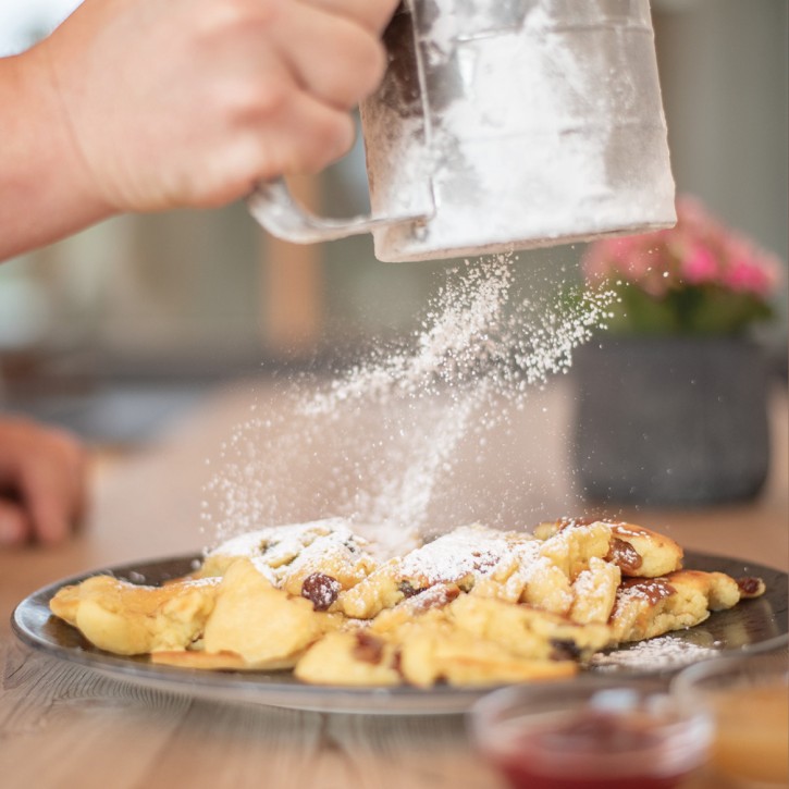 A tasty Kaiserschmarrn is currently being sprinkled with powdered sugar. The individual sugar particles are tumbling through the air.
