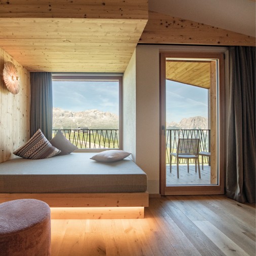 Bright, cozy room with wood-paneled walls and a large soft bed with several cuddly pillows in front of a window front.