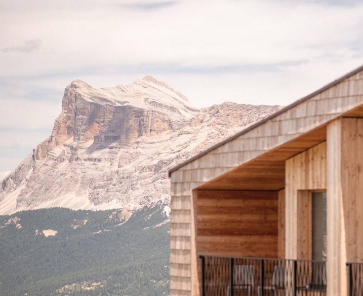 Imponente vetta montuosa nelle Dolomiti dietro il piano superiore del rifugio alpino Pralongià, che è rivestito con scandole di legno.
