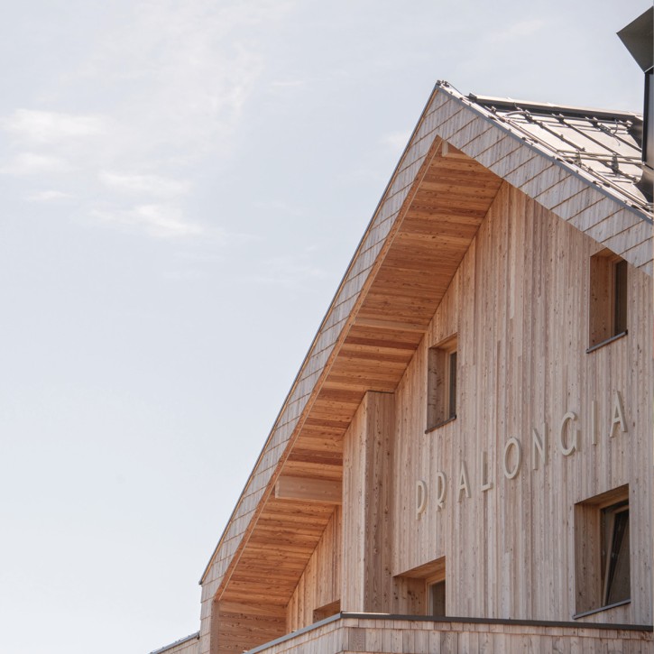 Close-up of the wood-paneled upper floor and roof of the newly renovated mountain inn with the Pralongià lettering.