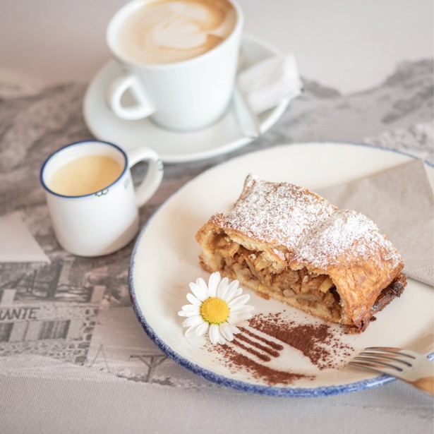 Un piatto di strudel di mele ben presentato, accompagnato da una tazza di caffè e salsa alla vaniglia.