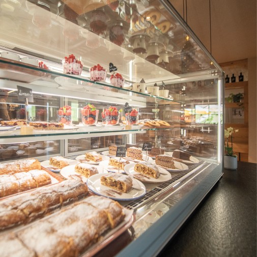 Glass display case with a large selection of desserts, including apple strudel and glasses with berries.