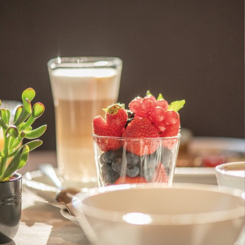 A glass full of wild berries in the middle of the set breakfast table, and a latte macchiato.