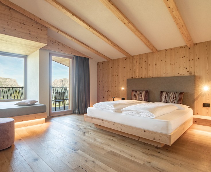 Camera da letto tranquilla con balcone e sedie, ampie vetrate portano molta luce nella stanza e il legno crea un'atmosfera piacevole. Vista sulle montagne imponenti.