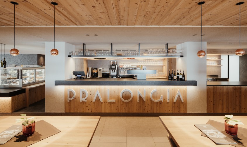Accogliente ristorante con bar; il bancone ha un frontale in legno vero e su di esso è montata una grande scritta Pralongià.