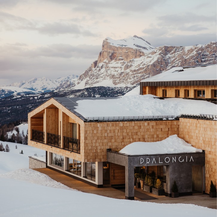 Das neu renovierte Berggasthaus Pralongià mit seiner Fassade aus Holzschindeln und beschneiten Dächern. Dolomitenberge im Hintergrund.