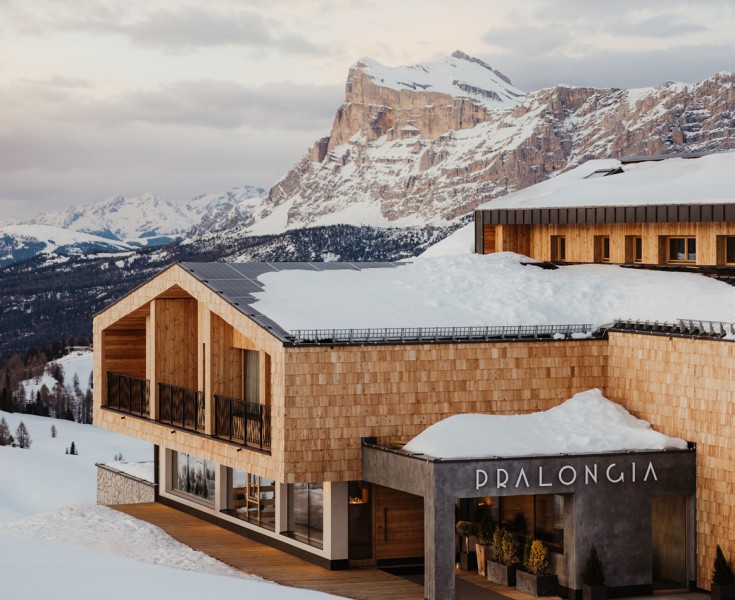 Il Rifugio Alpino Pralongià recentemente ristrutturato con la sua facciata in scandole di legno e tetti innevati. Montagne dolomitiche sullo sfondo.