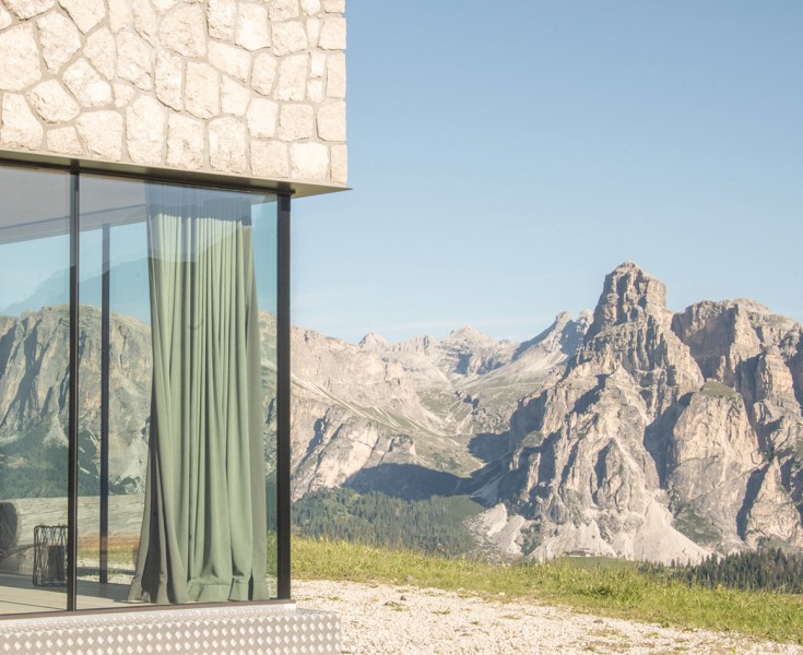Una delle tante vetrate viste dall'esterno. Lo sguardo passa in parte attraverso di essa e si posa sul massiccio paesaggio montano delle Dolomiti.