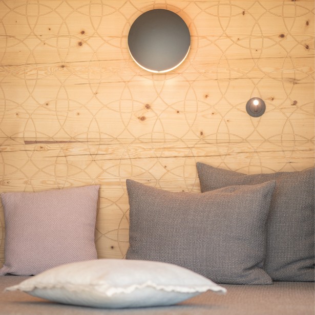 Sitzgelegenheit mit mehreren weichen Kissen vor einer Holzwand mit eingraviertem Muster.