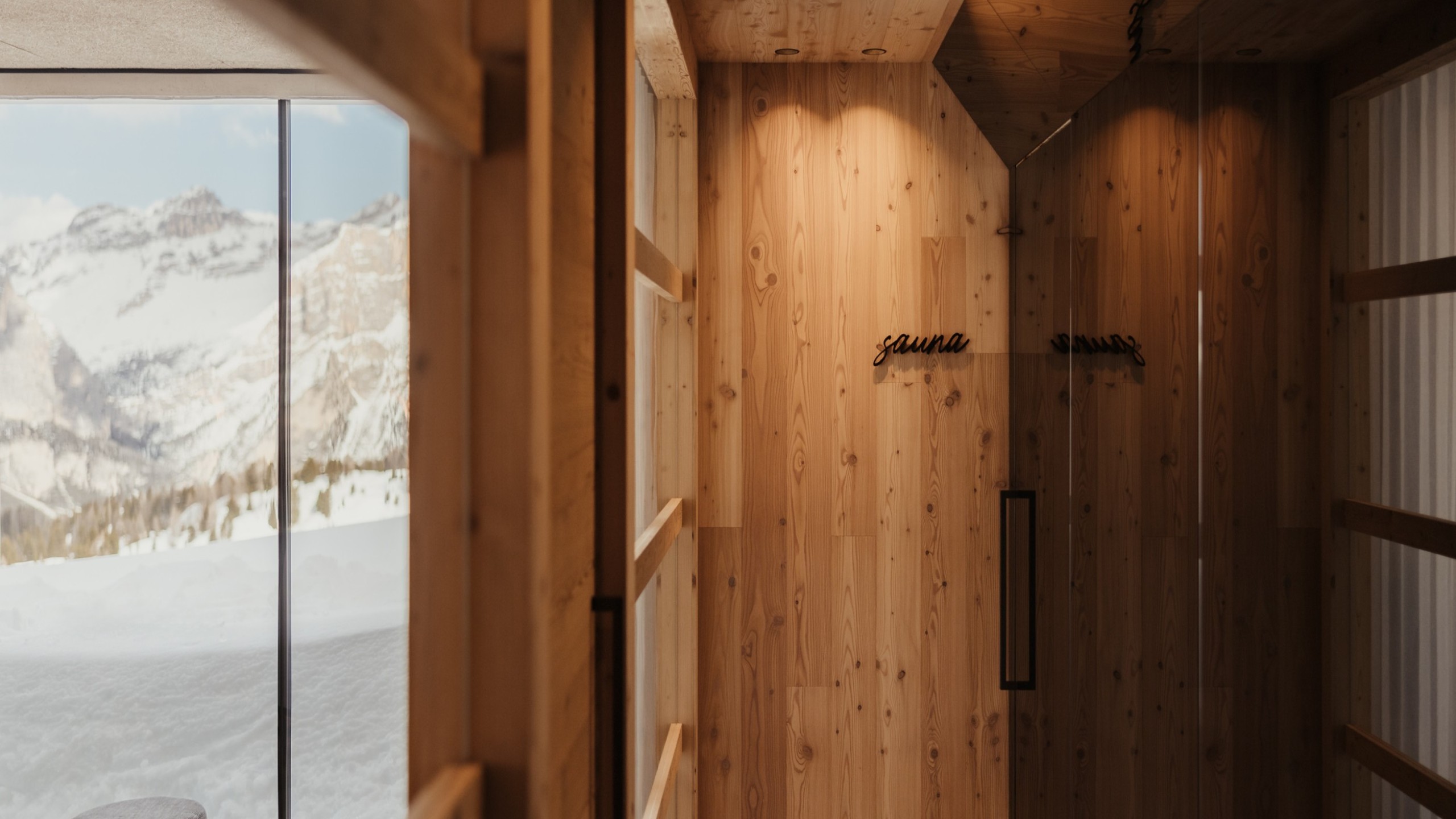 Holzwand mit dem Schriftzug sauna und durch einer Glastür Blick nach draußen auf verschneite Berge.