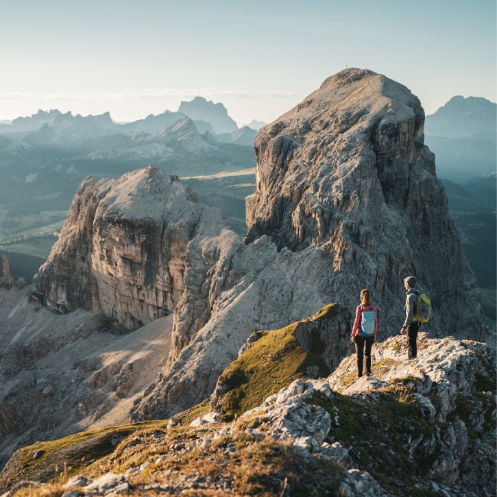 Two hikers are high up in the Dolomites, admiring the surrounding mountain landscape and also the neighboring peak.