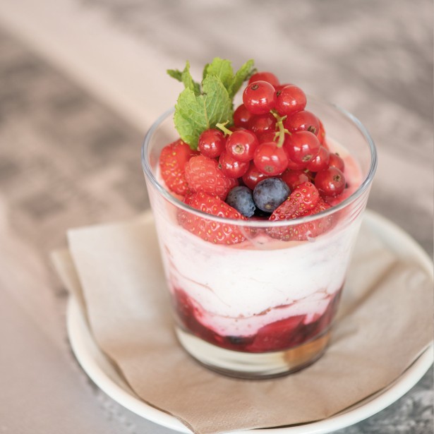 Un bicchiere pieno di frutti colorati, tra cui fragole, mirtilli e ribes rosso, servito con yogurt come delizioso dessert.