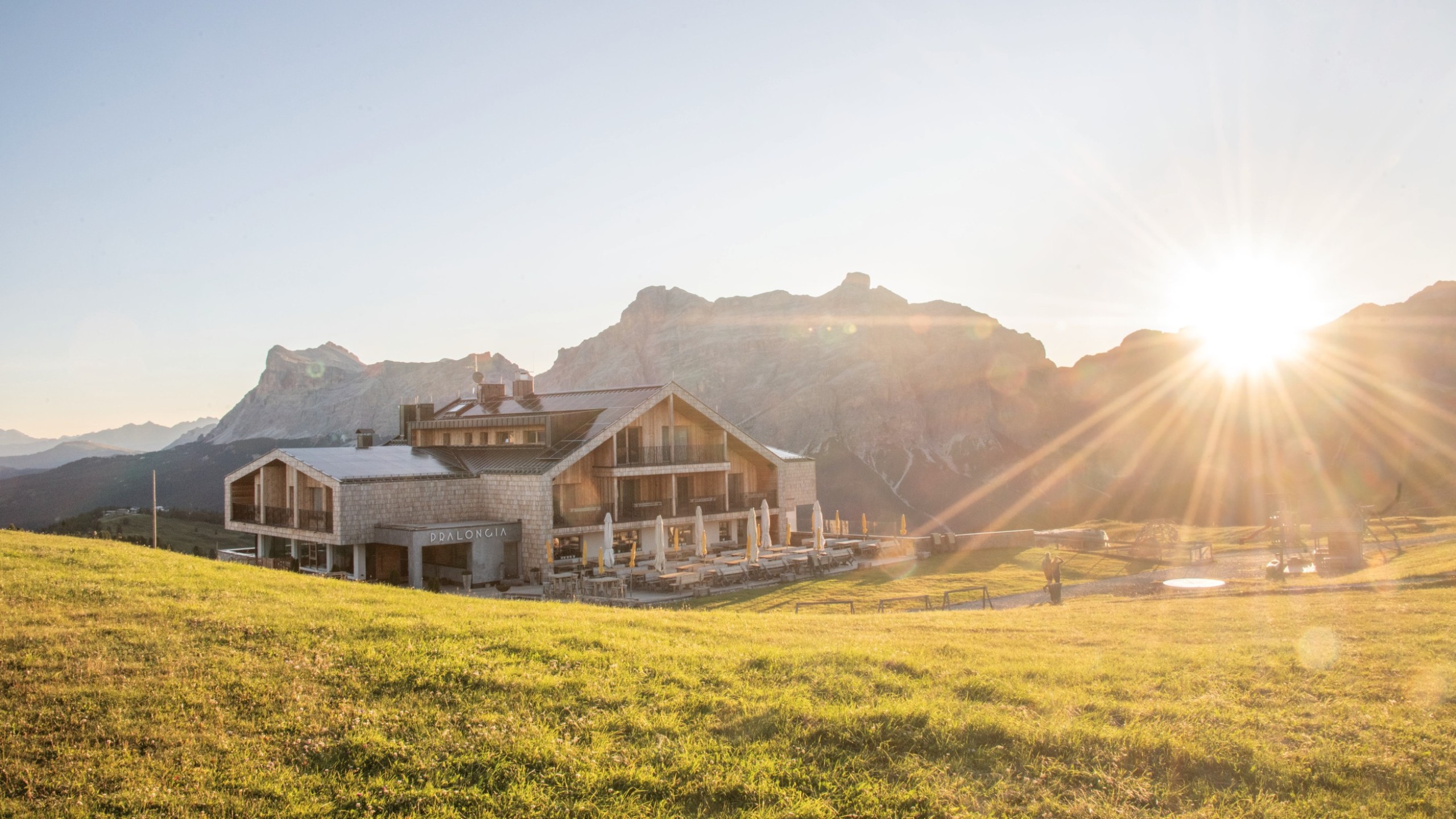 The Pralongià Mountain Inn in a wonderful solitary location on an early morning. The first sun rays fall on the surrounding meadow, with a prominent Dolomite mountain in the background.