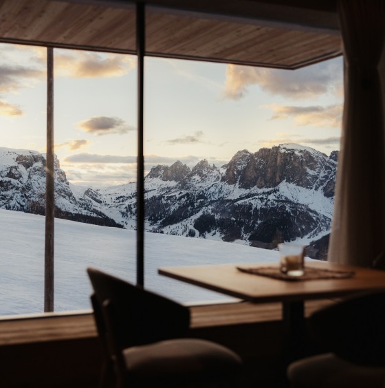 Un tavolo nella sala da pranzo proprio accanto a una vetrata che offre la vista sul panorama mozzafiato delle Dolomiti.