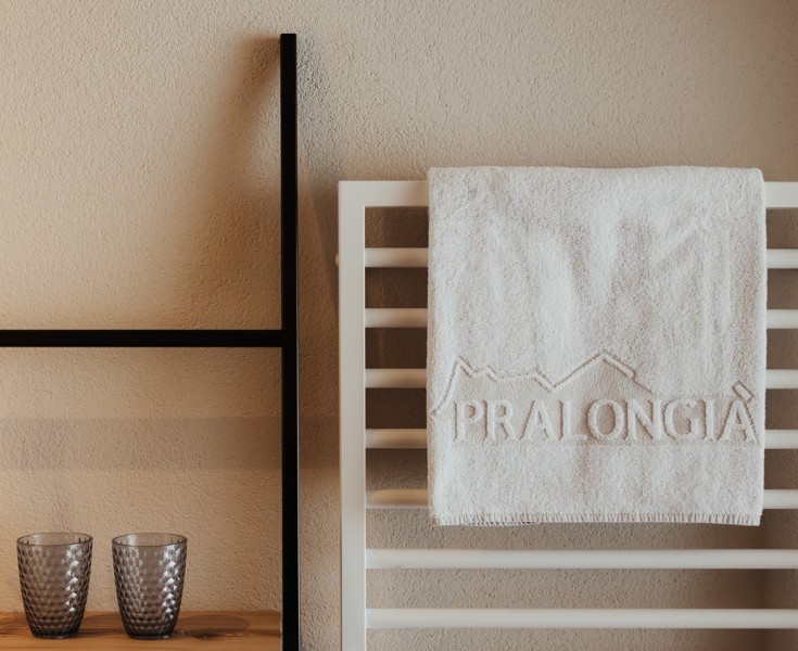 Un asciugamano fresco su un portasciugamani, accanto a una mensola con due bicchieri.