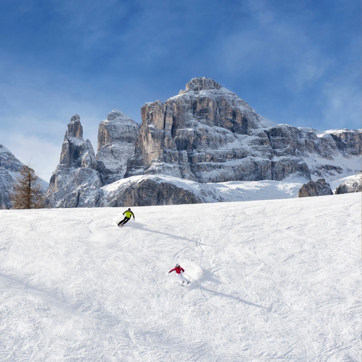 Zwei Skifahrer gönnen sich Pistengenuss an einem sonnigen Wintertag unter den Gipfeln der Dolomiten.