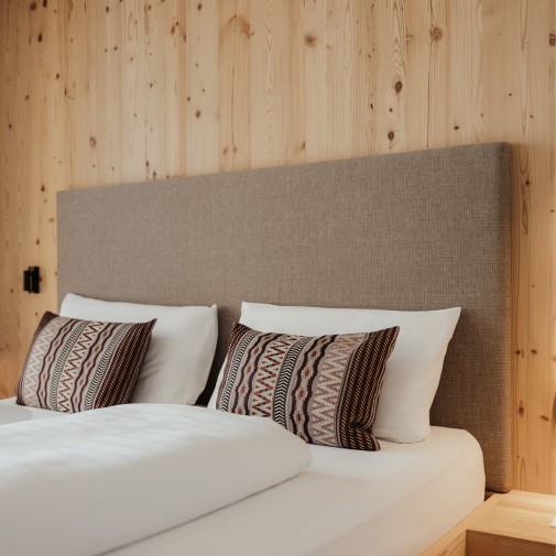 Im Zimmer ist das Kopfteil des Bettes mit Stoff überzogen, die Verkleidung der Wand besteht aus reinem Holz.