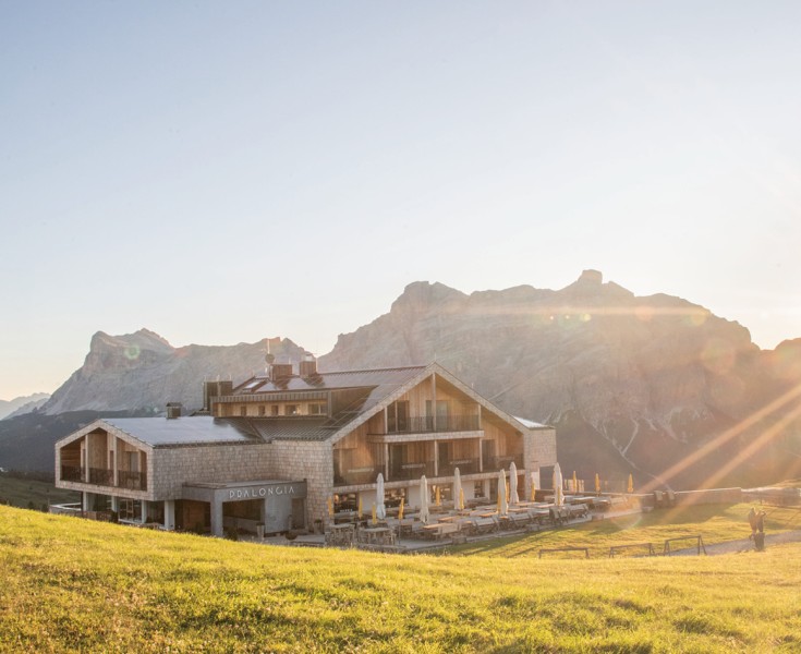 Il Rifugio Alpino Pralongià in una splendida posizione isolata in una mattina presto. I primi raggi di sole cadono sul prato circostante, con un'imponente montagna dolomitica sullo sfondo.