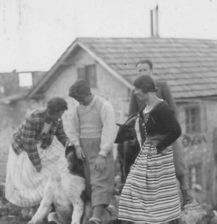 Old black-and-white photo with several laughing people and a large dog standing in front of the old Pralongià mountain inn.
