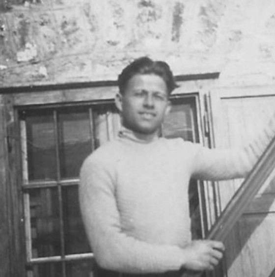 One of the brothers and founders of Pralongià is standing, grinning, in front of the window of the old mountain inn on a steep wooden staircase.