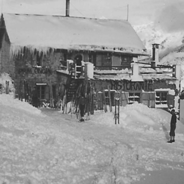 Old black-and-white photo of the first Pralongià mountain inn in winter. It is covered with a lot of snow.